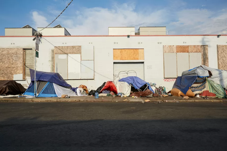 Small tents set up on sidewalk by unhoused people next to boarded-up one-story industrial building in San Francisco, California.